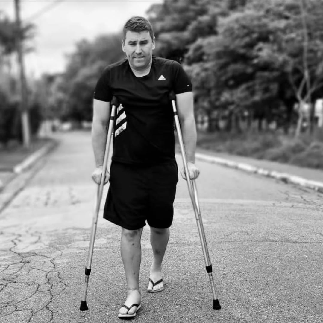 Caio caminhando de muletas, em preto e branco